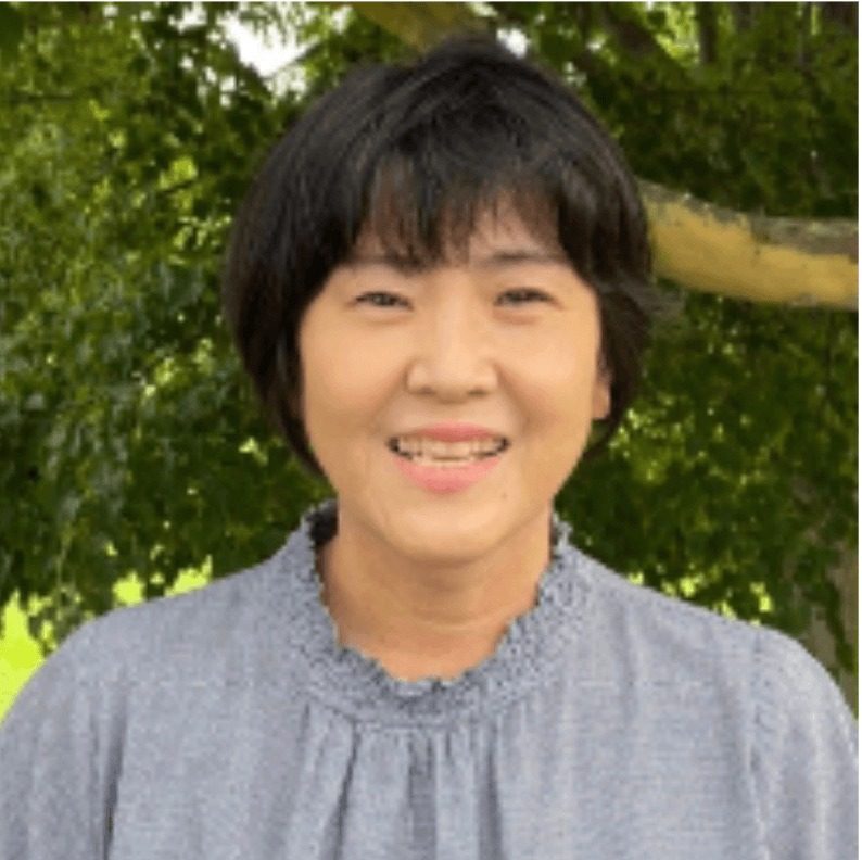 緑を背に笑顔で立つ最知紀子